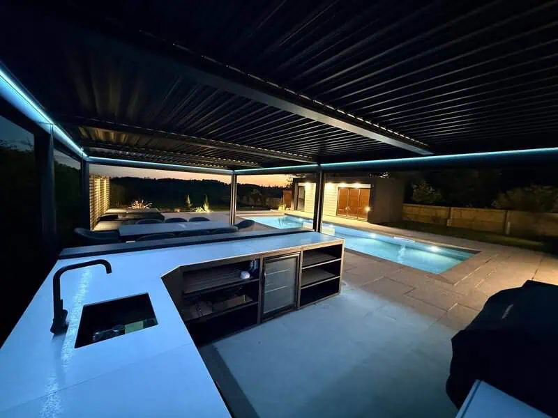 Covered outdoor kitchen and poolside entertaining space at night